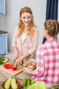 Josie the Chef cooking with a young girl in a bright kitchen, preparing fresh vegetables like bell peppers and mushrooms for a healthy family-friendly recipe.