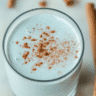 Glass of Blue Salt Trick drink topped with cinnamon powder, styled with cinnamon sticks on a marble background.