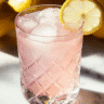 The pink salt detox drink in a crystal glass with a lemon slice, placed on a marble surface with whole lemons in the background.