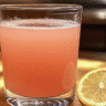 The Pink Salt Trick Recipe in a clear glass with half a lemon on a wooden kitchen counter.