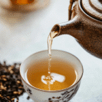 Japanese Green Tea Hojicha: The Ultimate Guide to This Roasted Delight 5 Close-up of Japanese Green Tea Hojicha being poured from a rustic ceramic teapot into a traditional floral teacup, with loose hojicha leaves in the background.