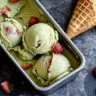 Melting matcha strawberry ice cream cone lying in a loaf pan with drips and visible berry chunks.