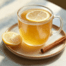 Clear glass mug filled with golden natural Ozempic juice topped with a lemon slice, next to cinnamon sticks on a white marble table.