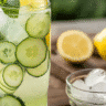 A tall glass of natural zepbound recipe with cucumber slices, lemon, fresh mint, and ice cubes on a wooden table.