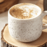 Hojicha latte served in a speckled ceramic mug on a wooden coaster with warm lighting.