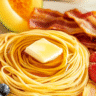 Plate of spaghetti pancake recipe with syrup and butter, served with crispy bacon and fresh fruit.