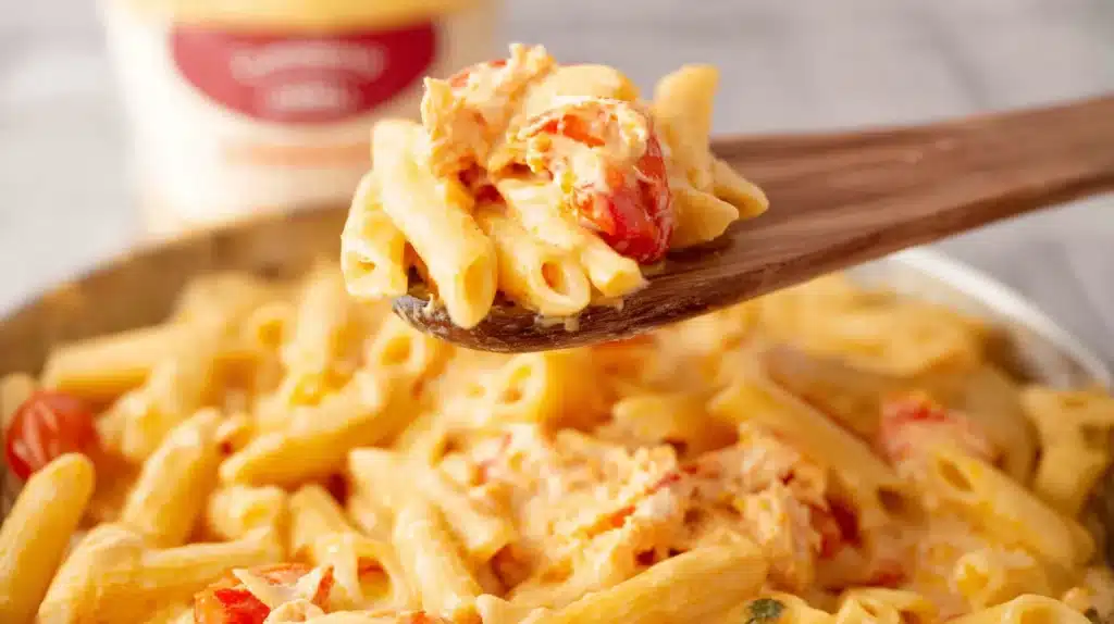 Close-up of creamy Trader Joes Lobster Pasta with penne, lobster chunks, and tomatoes on a wooden spoon.