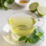 Lemon Balm Tea for Weight Loss Recipe: A Natural Herbal Slimming Solution 6 A glass teacup filled with lemon balm tea for weight loss recipe, garnished with fresh lemon balm leaves and served with lime halves and honey on a light surface.