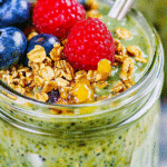 Close-up of matcha overnight oats in a mason jar topped with blueberries, raspberry, granola, and honey drizzle.