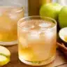 A glass of apple cider vinegar for weight loss recipe with ice, cinnamon, green apple, and lemon slices on a wooden table.