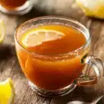 Costa Rican Tea Recipe: A Traditional Drink with Modern Benefits 5 A warm glass cup of Costa Rican Tea Recipe with a slice of lemon, served on a rustic wooden table with a spoon nearby.