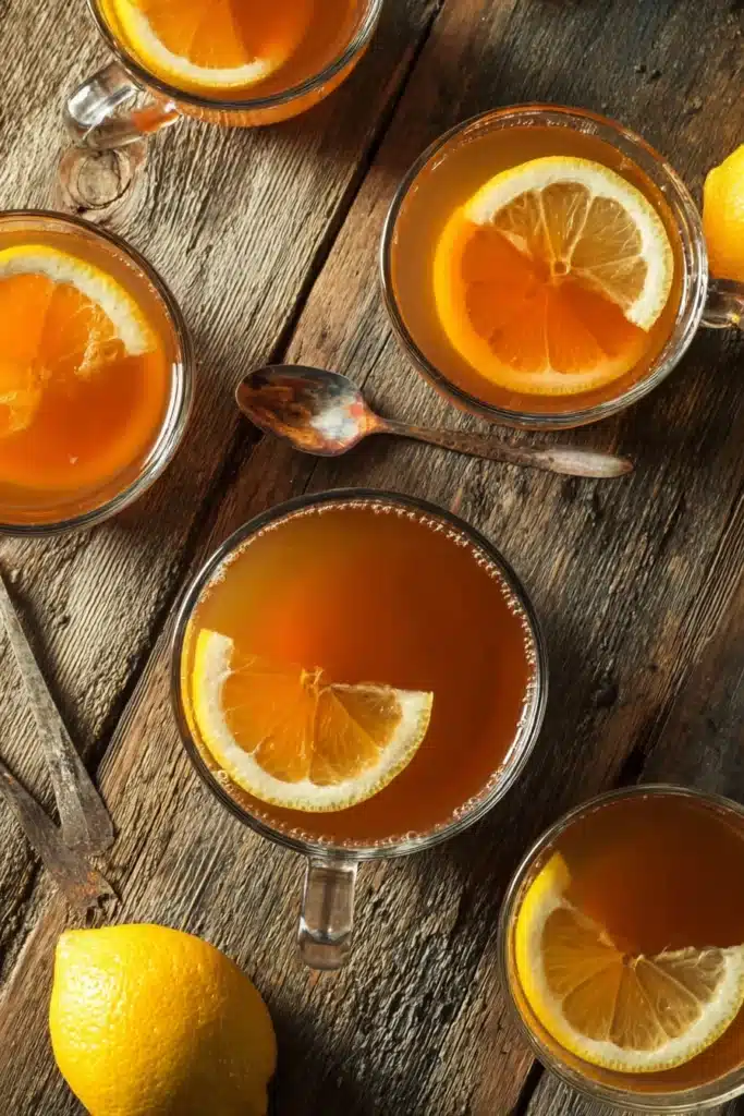 Costa Rican Tea Recipe: A Traditional Drink with Modern Benefits 6 Overhead view of multiple glass cups filled with Costa Rican Tea Recipe, garnished with lemon slices on a rustic wooden table.