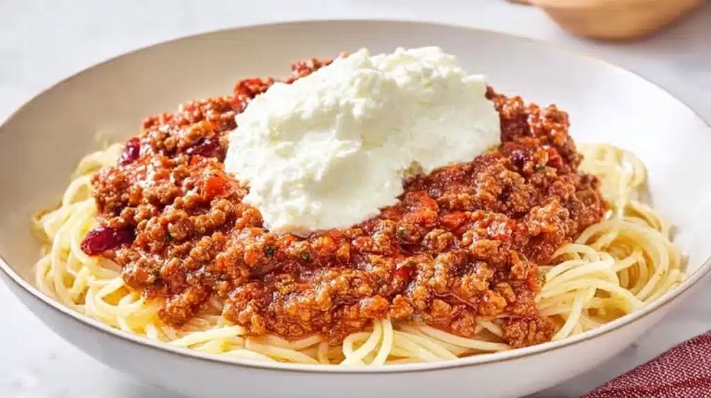 A bowl of Cranberry Spaghetti topped with cranberry-infused meat sauce and a scoop of ricotta cheese.