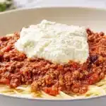 A bowl of Cranberry Spaghetti topped with cranberry-infused meat sauce and a creamy dollop of ricotta cheese.