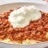 A bowl of Cranberry Spaghetti topped with cranberry-infused meat sauce and a scoop of ricotta cheese.