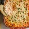 Close-up of a freshly baked Marry Me Chicken Dip Recipe in a ceramic dish, topped with golden melted cheese and fresh herbs.