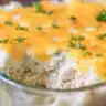 Golden turkey and mashed potatoes casserole topped with melted cheddar cheese and fresh parsley in a glass baking dish.