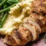 Garlic butter turkey tenderloin served with mashed potatoes and sautéed green beans, garnished with rosemary on a rustic plate.