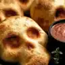 Golden-brown Halloween pizza skulls served with marinara dipping sauce on a black plate.