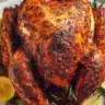 Perfectly roasted Thanksgiving turkey with crispy golden skin, garnished with lemon wedges and fresh rosemary on a white serving platter.