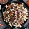 Halloween popcorn mix with candy eyeballs, colorful sprinkles, chocolate drizzle, and candy pumpkins in a black bowl on a spiderweb tablecloth.