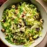 Shaved Brussels sprouts salad with dried cranberries, hazelnuts, and Parmesan shavings served in a ceramic bowl.