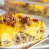 A slice of sausage breakfast casserole topped with melted cheddar and crumbled sausage on a white plate.
