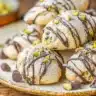Cannoli cookies drizzled with chocolate and dusted with powdered sugar on a ceramic plate with pistachios.