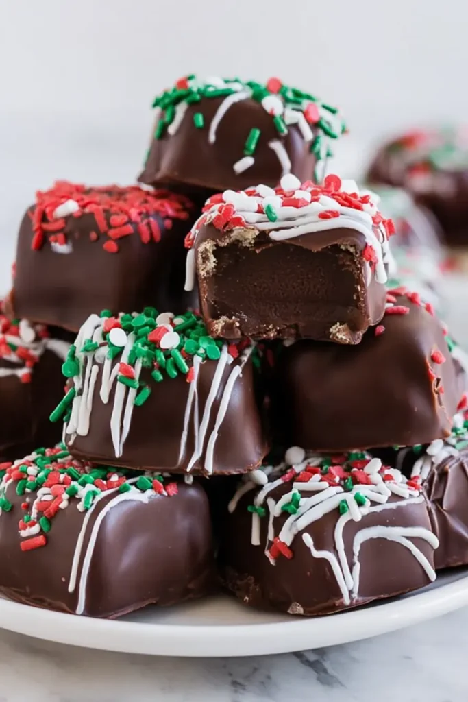 Stack of chocolate-coated Cool Whip Candy pieces decorated with red, green, and white sprinkles on a white plate.