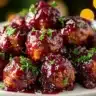 A plate of cranberry-glazed meatballs garnished with fresh parsley, with warm holiday lights blurred in the background.
