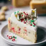 A rich and creamy sugar cookie cheesecake topped with vanilla frosting and festive Christmas sprinkles.