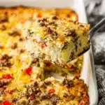 A serving of breakfast casserole with hashbrowns, eggs, sausage, and melted cheese lifted from a baking dish.