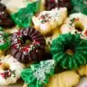 A plate of colorful Christmas spritz cookies decorated with chocolate, icing, and festive red and green sprinkles.