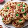 Christmas kitchen sink cookies topped with red and green M&Ms, pretzels, white chocolate chips, and sprinkles on a serving plate.