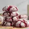 Stack of red velvet crinkle cookies dusted with powdered sugar on parchment paper.