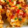 Slice of overnight breakfast casserole topped with melted cheese, crispy bacon, and diced peppers.