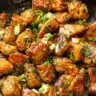 Golden garlic butter chicken bites in a skillet topped with parsley and green onions.