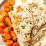 Plate of cream cheese chicken served with mashed potatoes and carrots topped with creamy sauce and parsley.