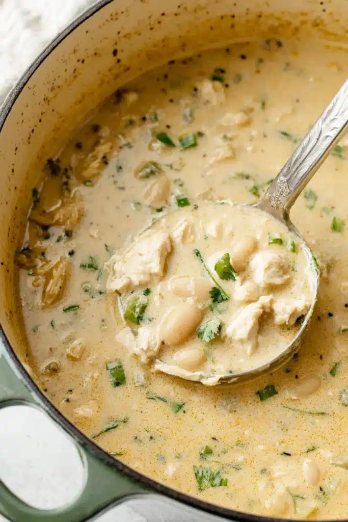 Creamy White Chicken Chili Soup A Cozy Healthy Dinner Ready Fast 7 Creamy white chicken chili soup in a Dutch oven with a ladle lifting tender chicken pieces, beans, and fresh herbs.
