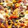 Santa Fe chicken topped with melted cheese surrounded by black beans, corn, tomatoes, and chiles in a skillet.