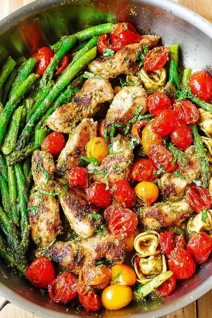 A colorful one-pan pesto chicken dish loaded with tender cheese tortellini, fresh asparagus, and juicy cherry tomatoes for an easy, flavorful dinner.