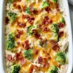 Low carb chicken casserole in a white baking dish topped with broccoli, melted cheddar cheese, and crispy bacon.