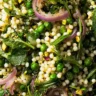 Spring couscous salad with pearl couscous, peas, arugula, mint, and red onions in a white bowl.