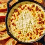 Skillet of baked garlic bread dip with a golden cheesy top surrounded by toasted baguette slices.