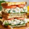 Lemon basil chicken salad sandwich stacked with creamy chicken filling, fresh basil, and tomato slices on toasted bread.