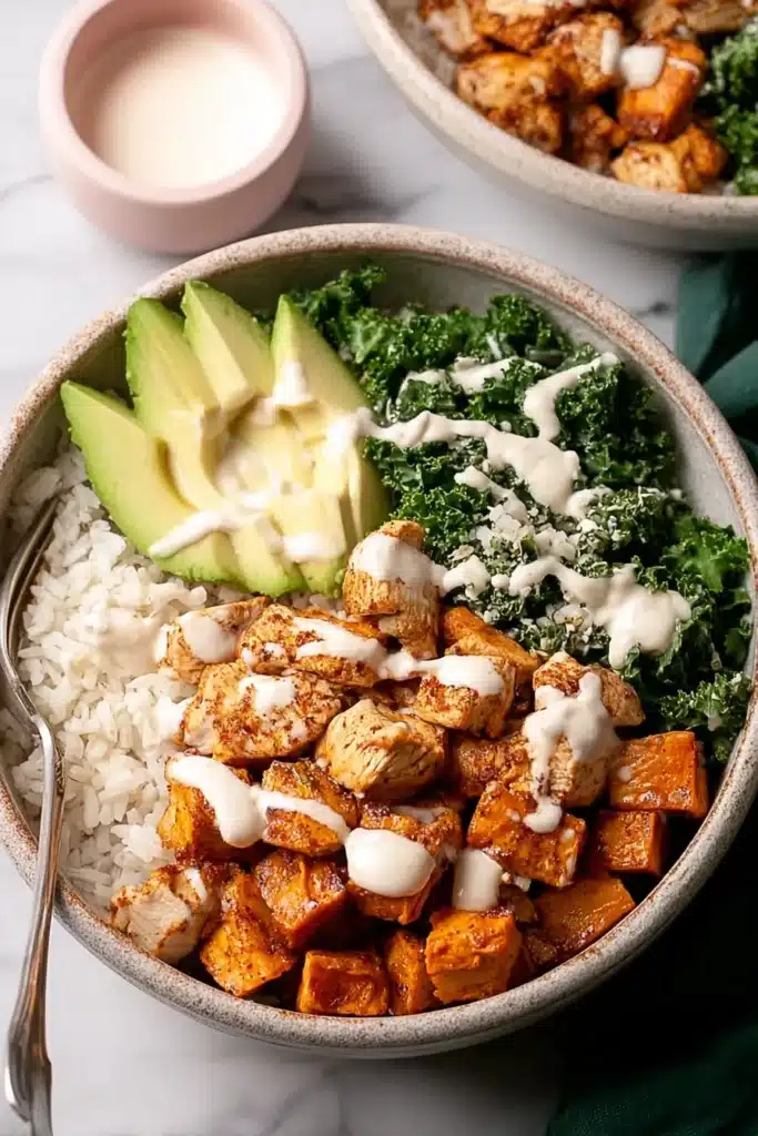 A nourishing chicken and sweet potato rice bowl topped with fresh kale, creamy avocado slices, and a smooth drizzle of sauce for the perfect balanced meal.