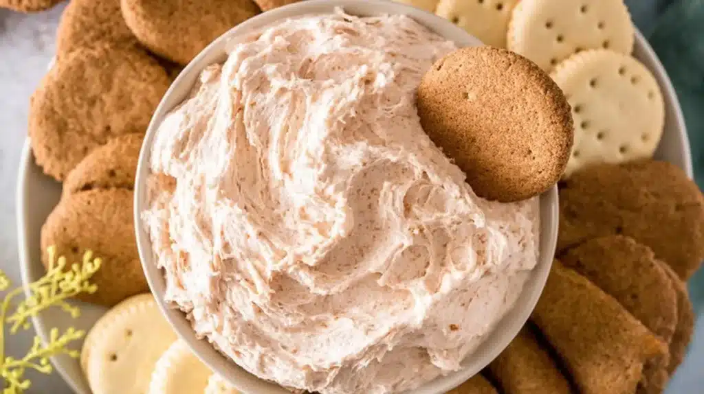 Fluffy cinnamon roll dip served in a bowl with ginger snaps, graham crackers, and cookies for dipping.
