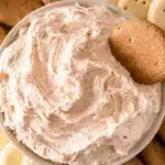 Fluffy cinnamon roll dip served in a bowl with ginger snaps, graham crackers, and cookies for dipping.